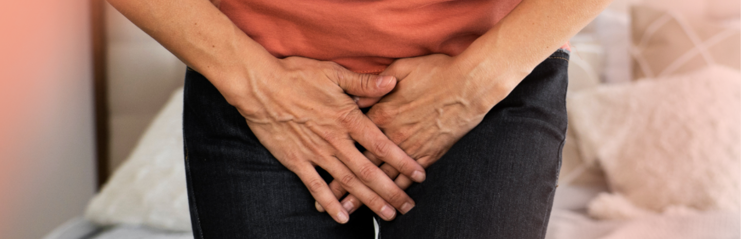A person in a red shirt holds their vagina, showing signs of discomfort, seated on a bed with soft bedding in the background.