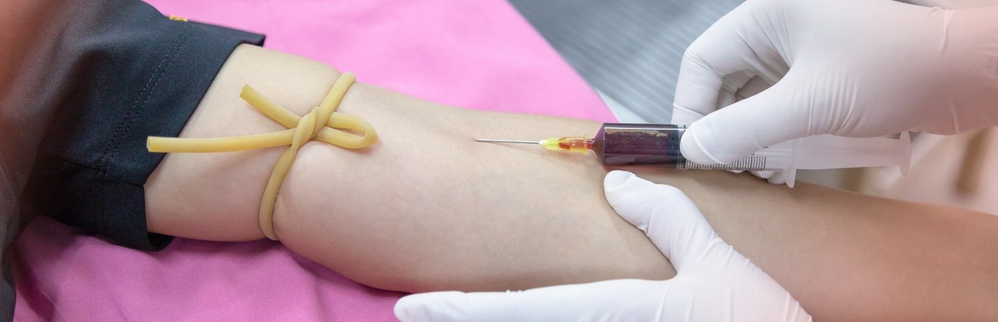 A healthcare professional draws blood from a patient's arm, using a syringe and tourniquet, on a pink examination table.