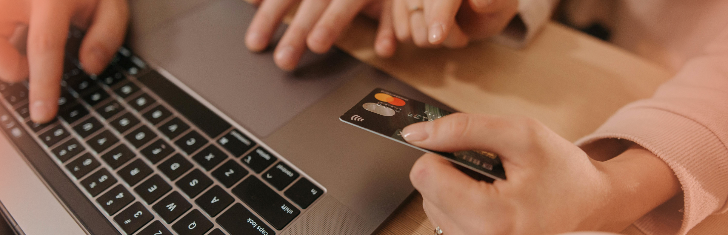 Hands hover over a laptop keyboard, one holding a credit card. The scene suggests online shopping or payment, conveying a sense of modern convenience.