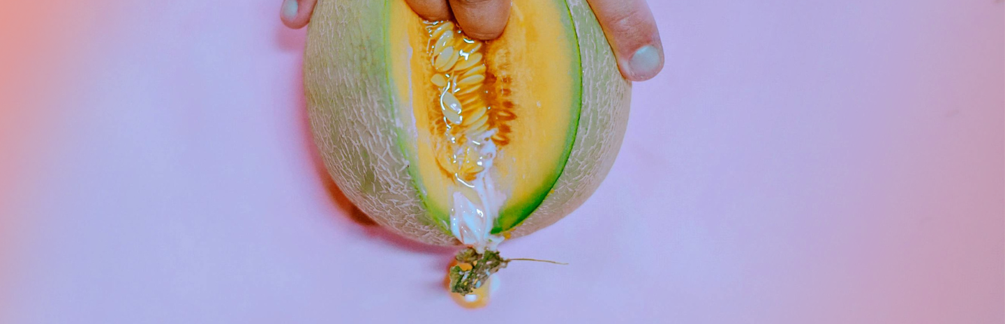 Close-up of a hand splitting open a melon with white fluid oozing out, symbolizing white discharge before your period on a pink background.