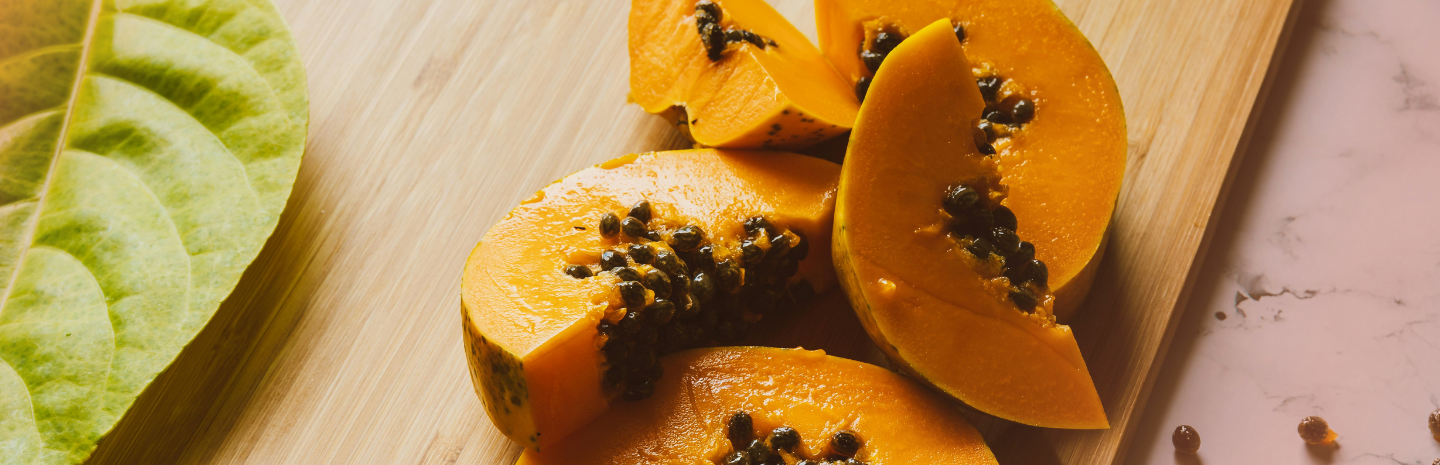 Sliced papaya on a wooden cutting board with a leaf in the background