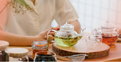 Person holding a glass teapot with tea on a wooden table