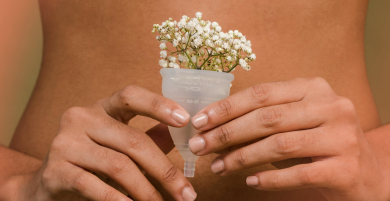 The image shows a person holding a menstrual cup with small white flowers inside.