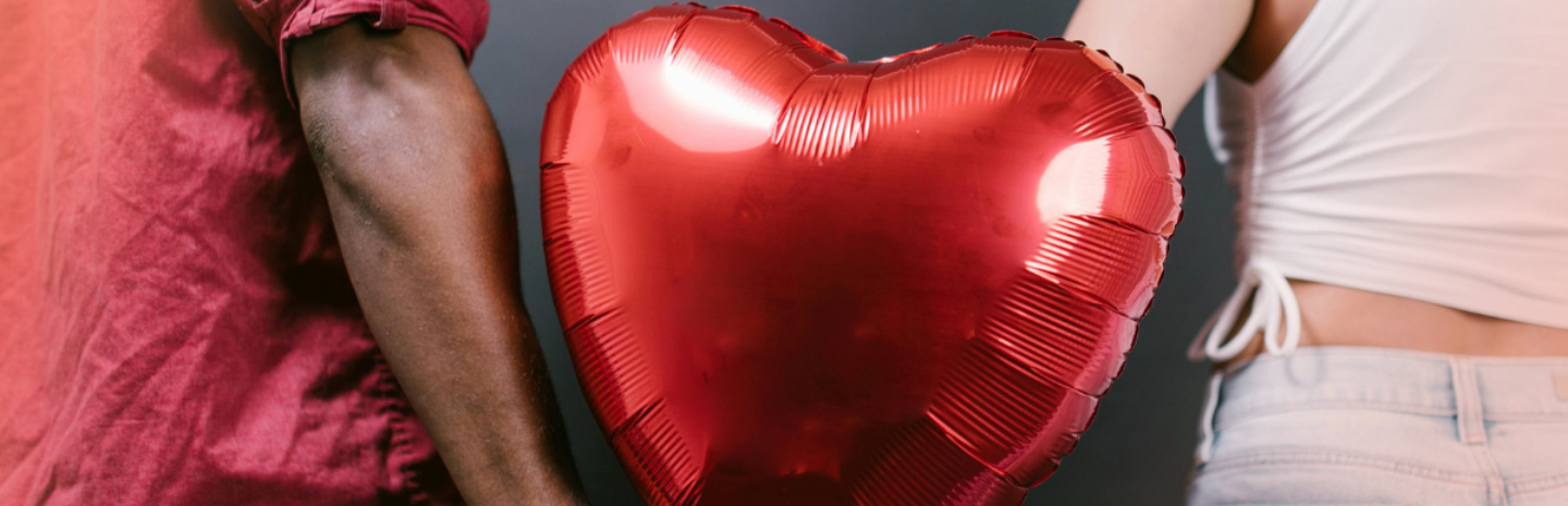 Two people holding a red heart-shaped balloon together.