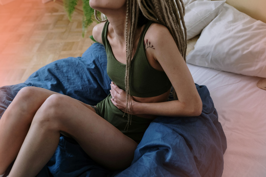 woman in green sits on a bed, clutching her stomach in period pain
