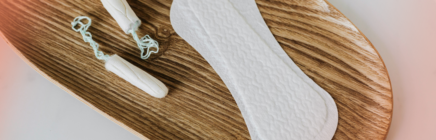 Tampons and a sanitary pad on a wooden tray, highlighting menstrual hygiene products. The setting is clean and minimal, conveying a sense of care and comfort.