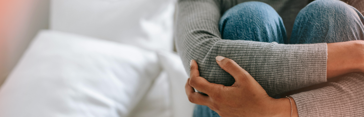 A person sitting on a bed, hugging their knees, suggesting stress, sadness, or deep thought.