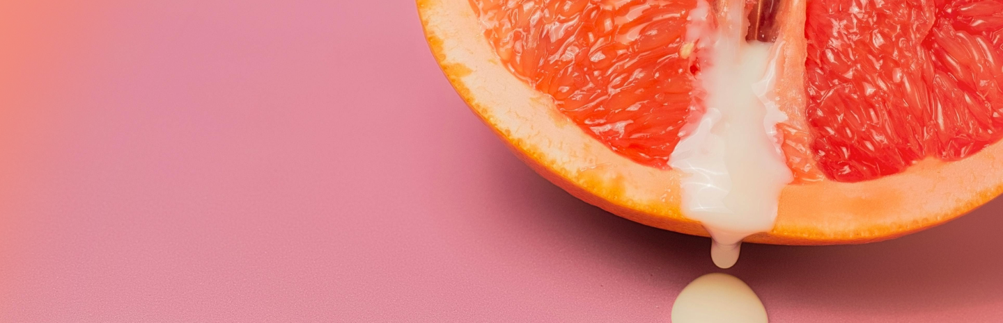 Close-up of a grapefruit half on a pink background. Creamy liquid drips from the fruit, creating a playful, vibrant, and slightly whimsical scene.