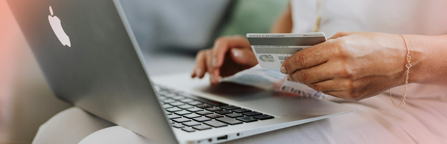 A person holds a credit card while typing on a laptop, suggesting online shopping or payment. The scene feels modern and convenient.