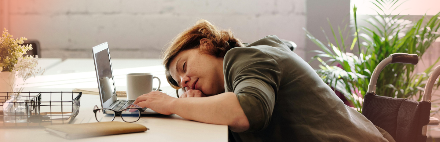 Person sleeping at a desk with a laptop and coffee cup