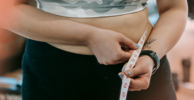 Person measuring waist with a tape measure in an indoor setting